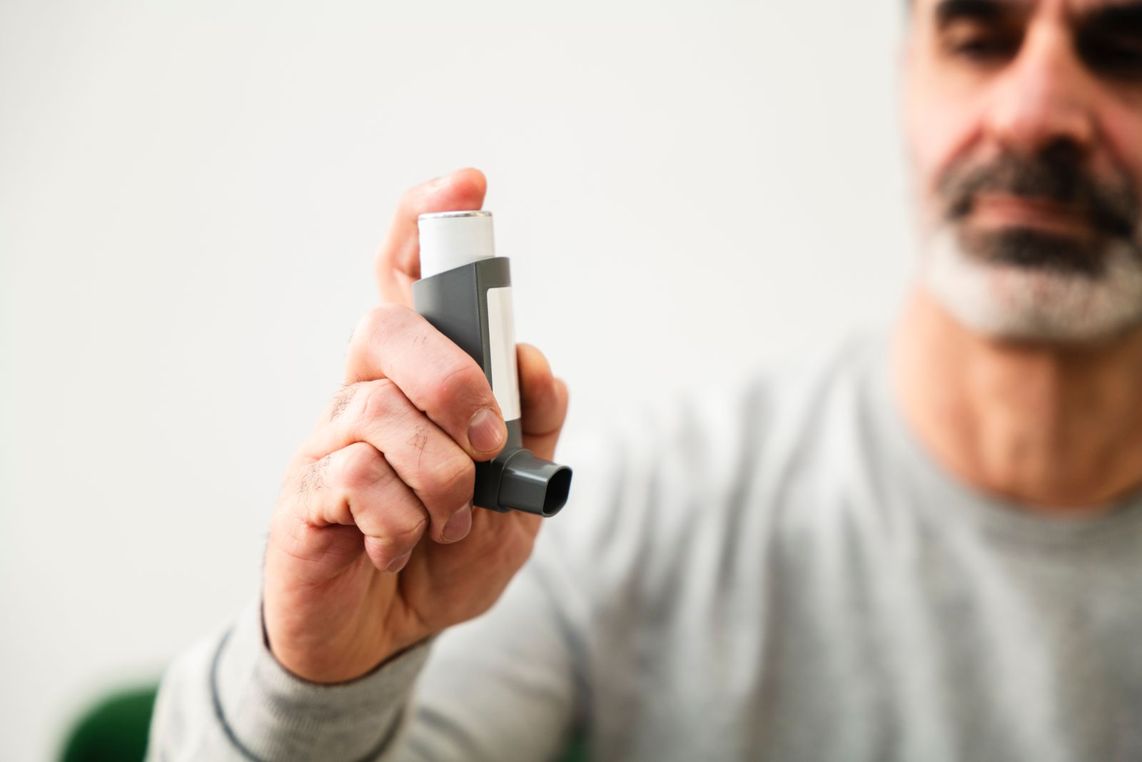 A man holding up a rescue inhaler used to manage asthma or COPD symptoms
