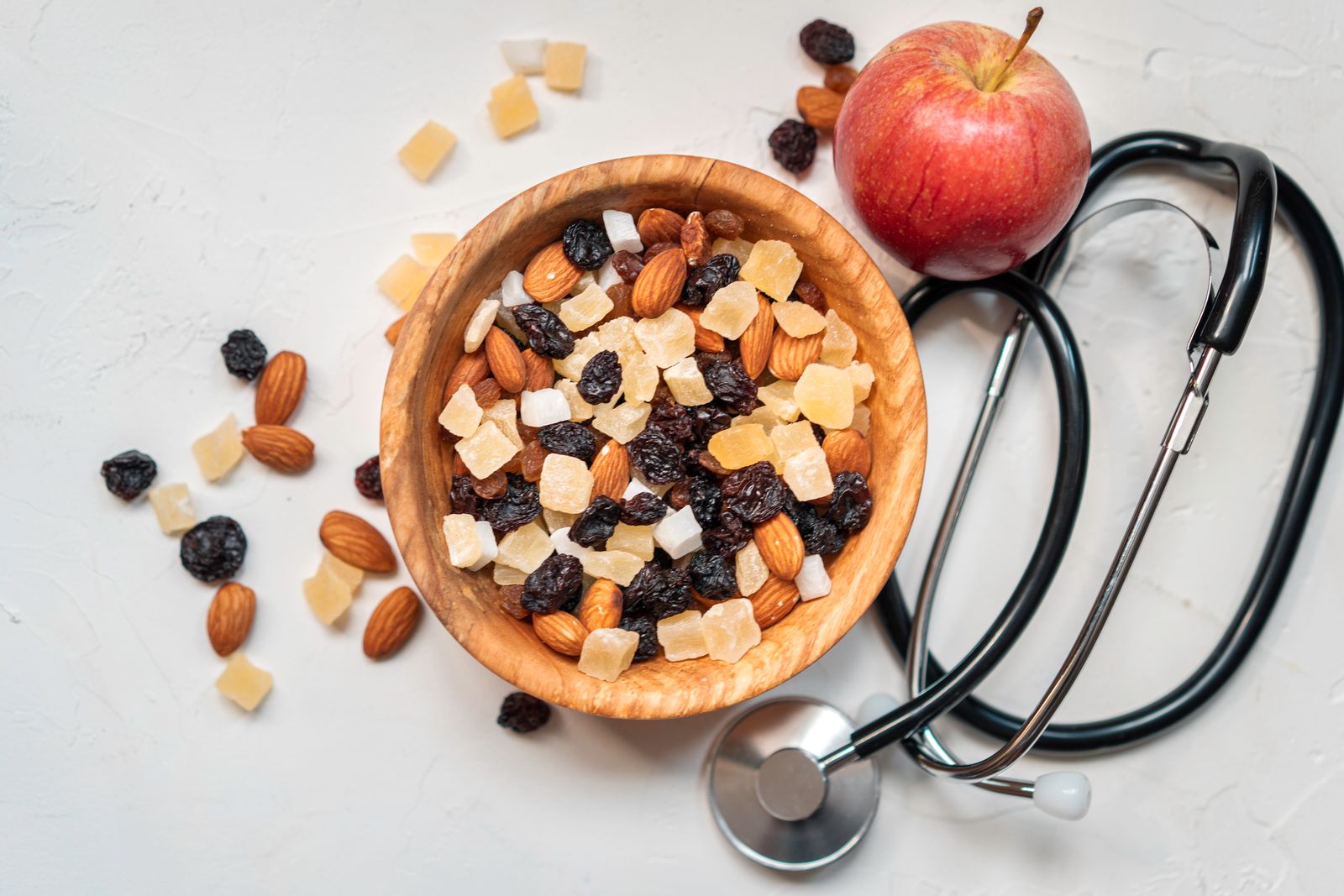 A flat-lay of a bowl of nuts and dried fruit, an apple, and a stethoscope, representing heart-healthy nutrition