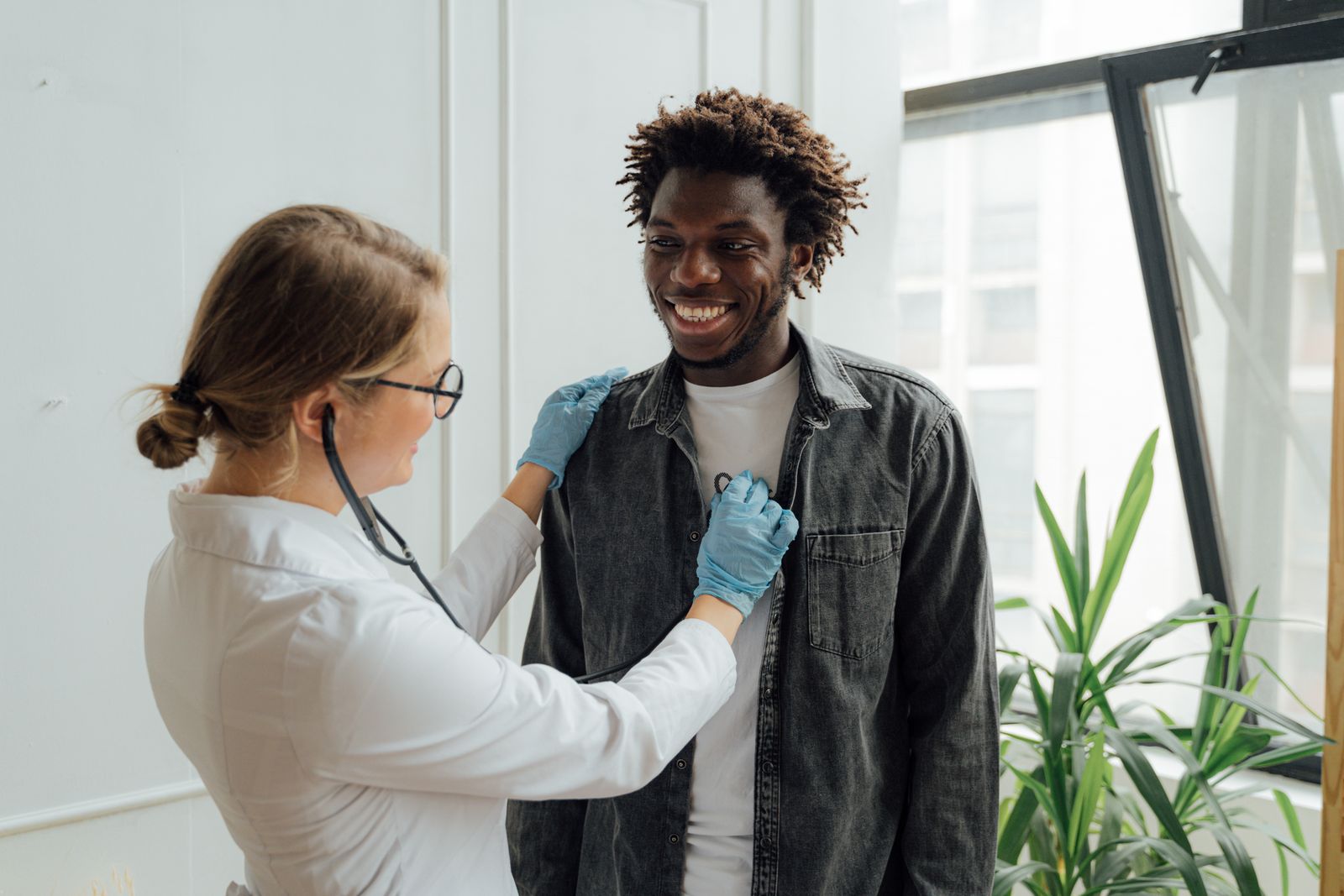 A physician using a stethoscope to examine a smiling patient during a same-day illness visit