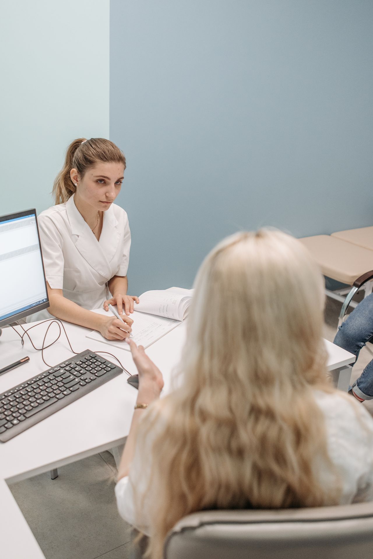 A healthcare provider taking notes at a desk during a preventive care visit with a patient