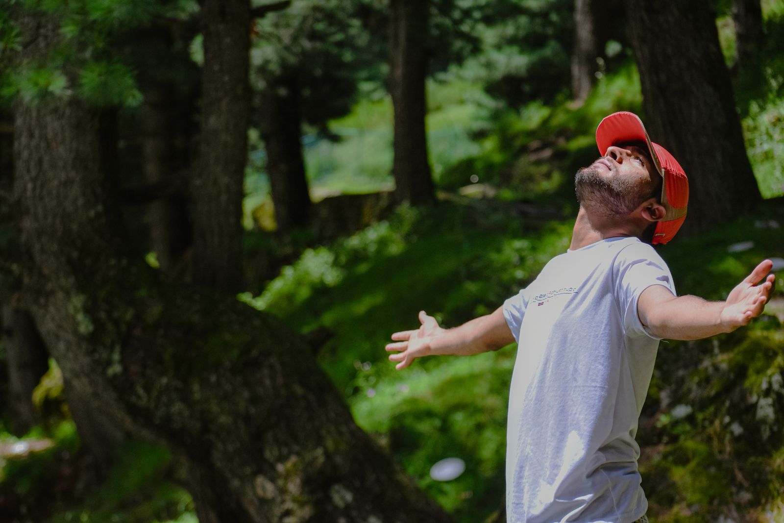 A man standing outdoors with arms outstretched, breathing freely in a wooded setting